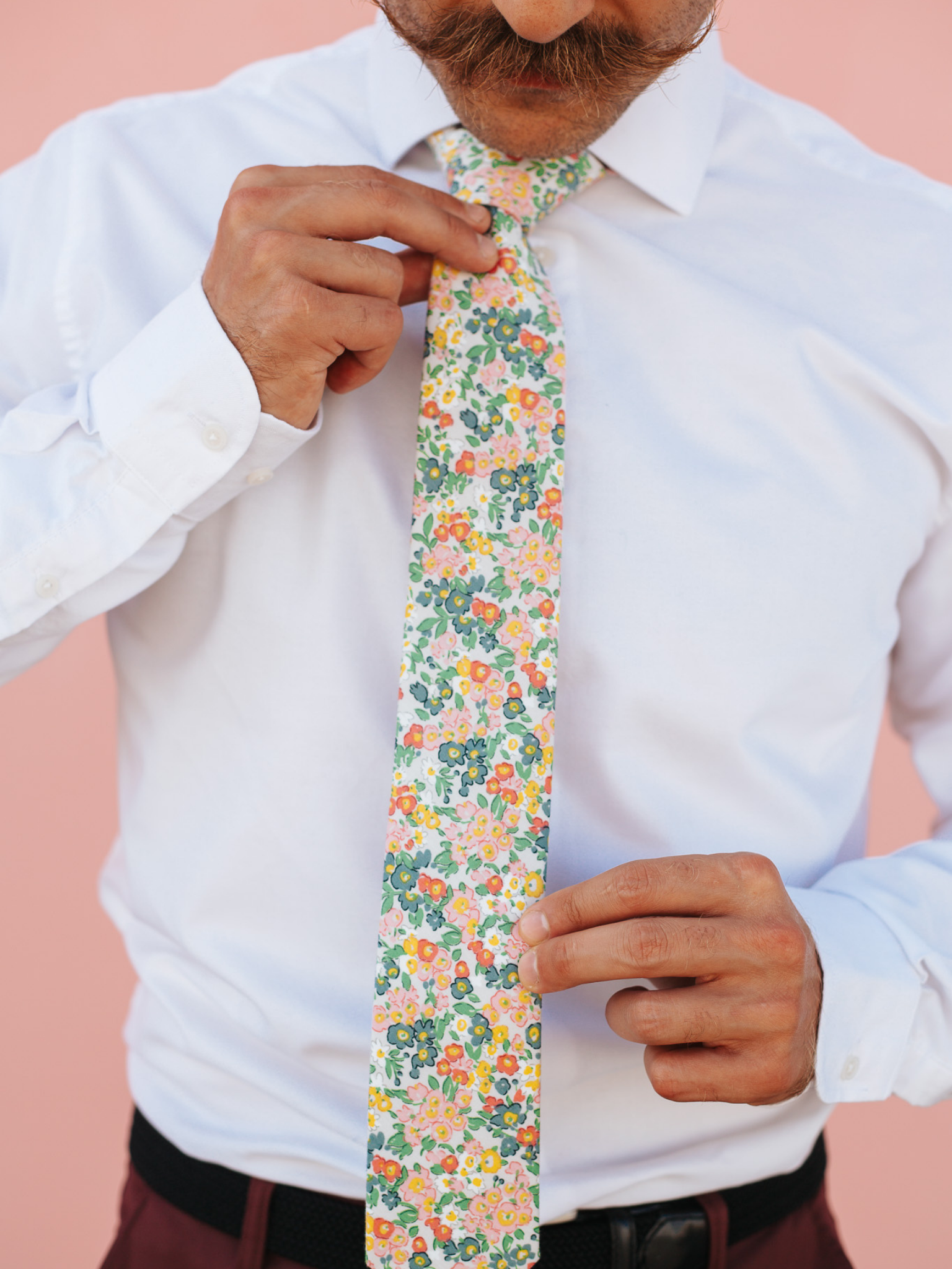 A close up of a man wearing a white and pink flower cotton skinny tie for weddings, grooms, and groomsmen.