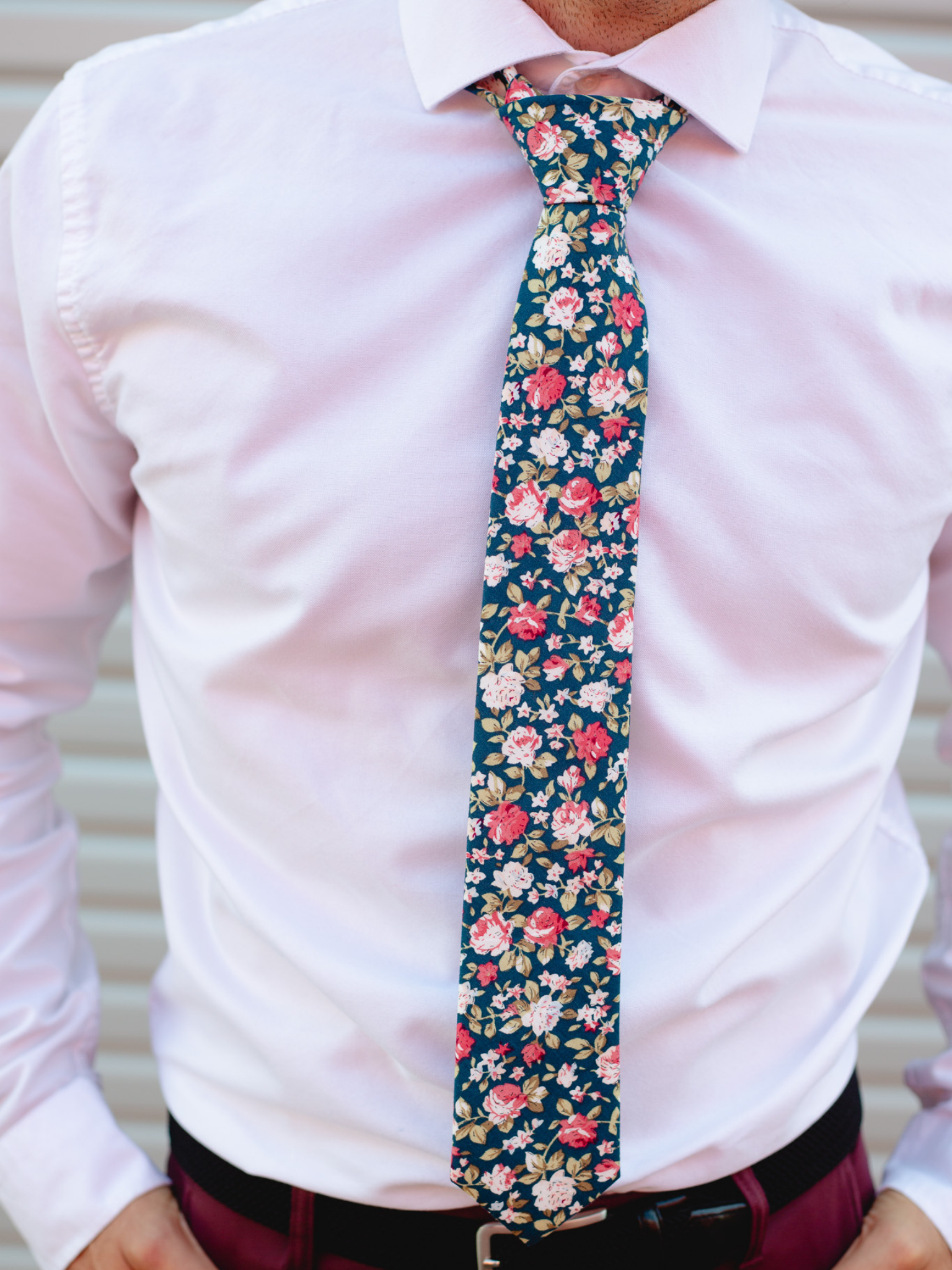 A close up of a man wearing a navy, red, and pink flower cotton skinny tie for weddings, grooms, and groomsmen.