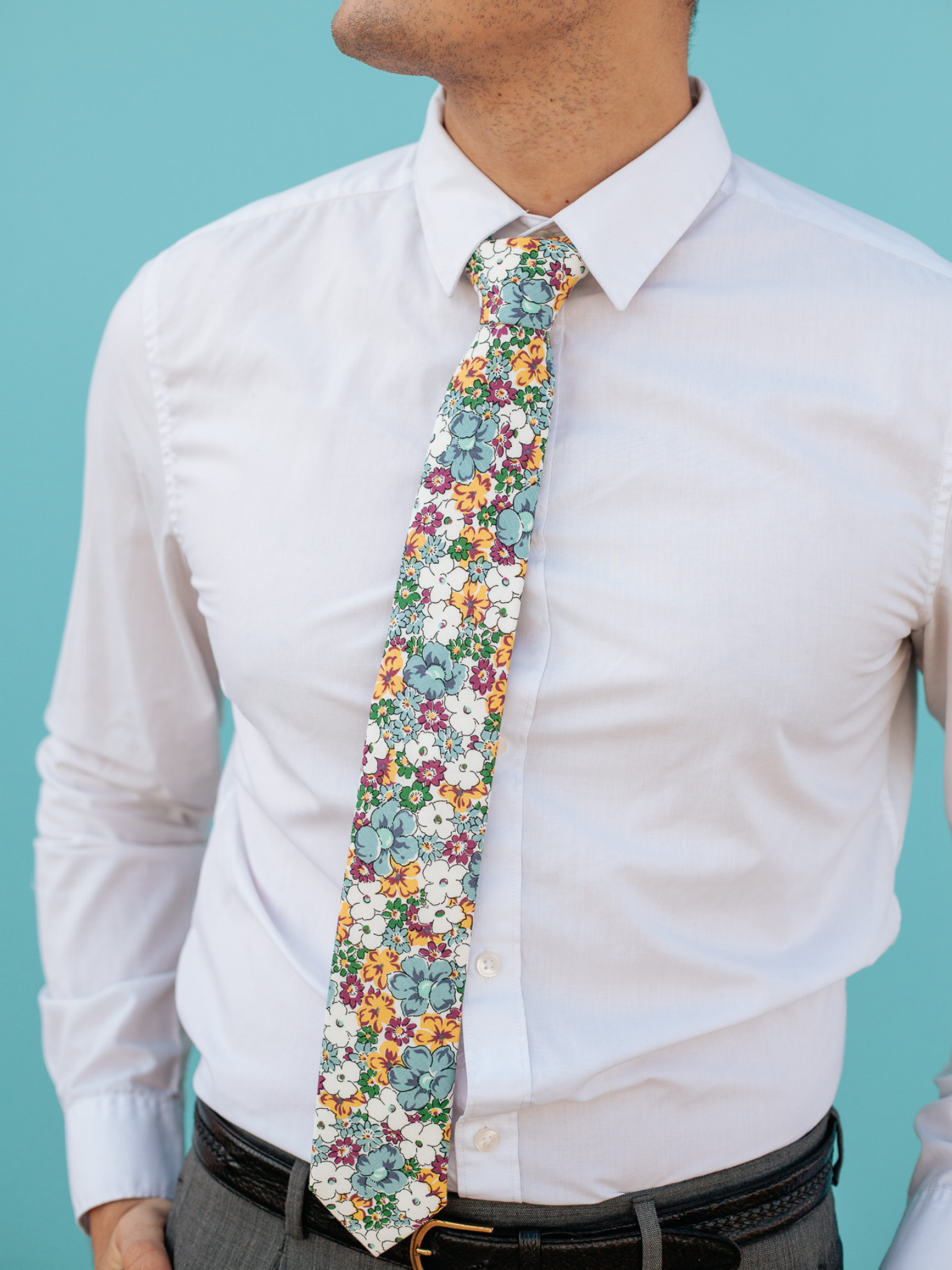 A close up of a man wearing a white, purple, and blue flower cotton skinny tie for weddings, grooms, and groomsmen.