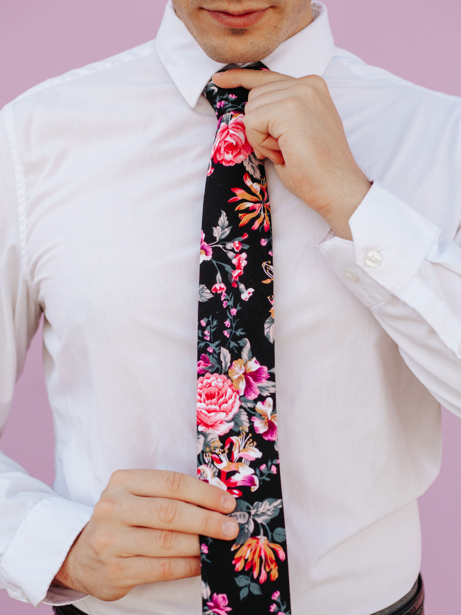 A close up of a man wearing a black and pink flower cotton skinny tie for weddings, grooms, and groomsmen.