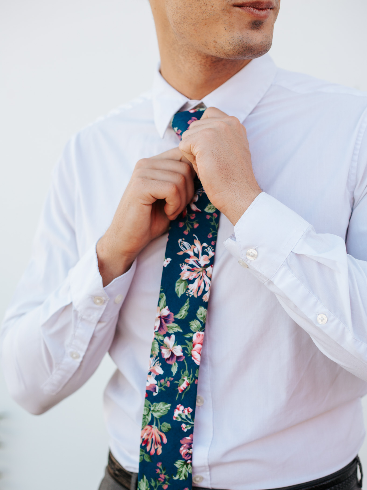 A close up of a man wearing a navy, green, and pink flower cotton skinny tie for weddings, grooms, and groomsmen.