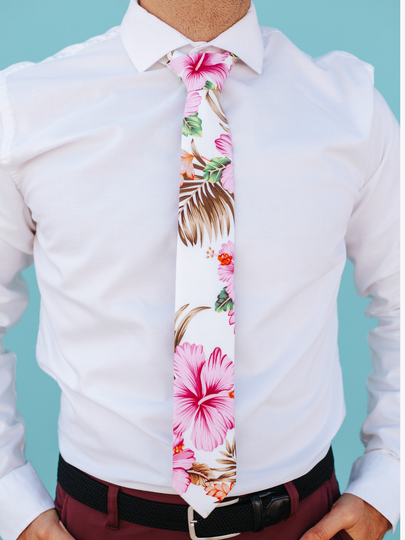 A close up of a man wearing a white, brown, and pink flower cotton skinny tie for weddings, grooms, and groomsmen.