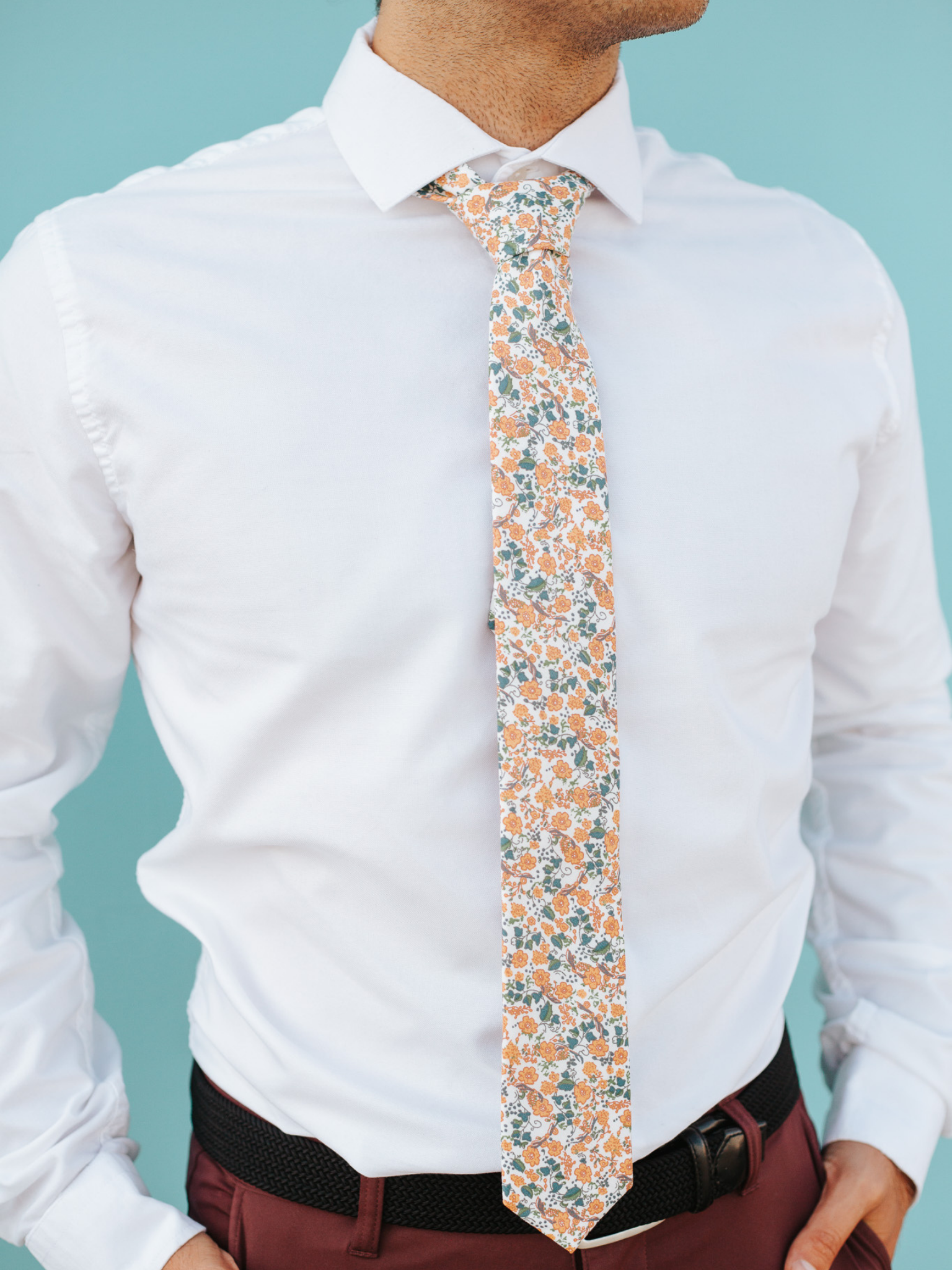 A close up of a man wearing a white, blue  and orange flower cotton skinny tie for weddings, grooms, and groomsmen.