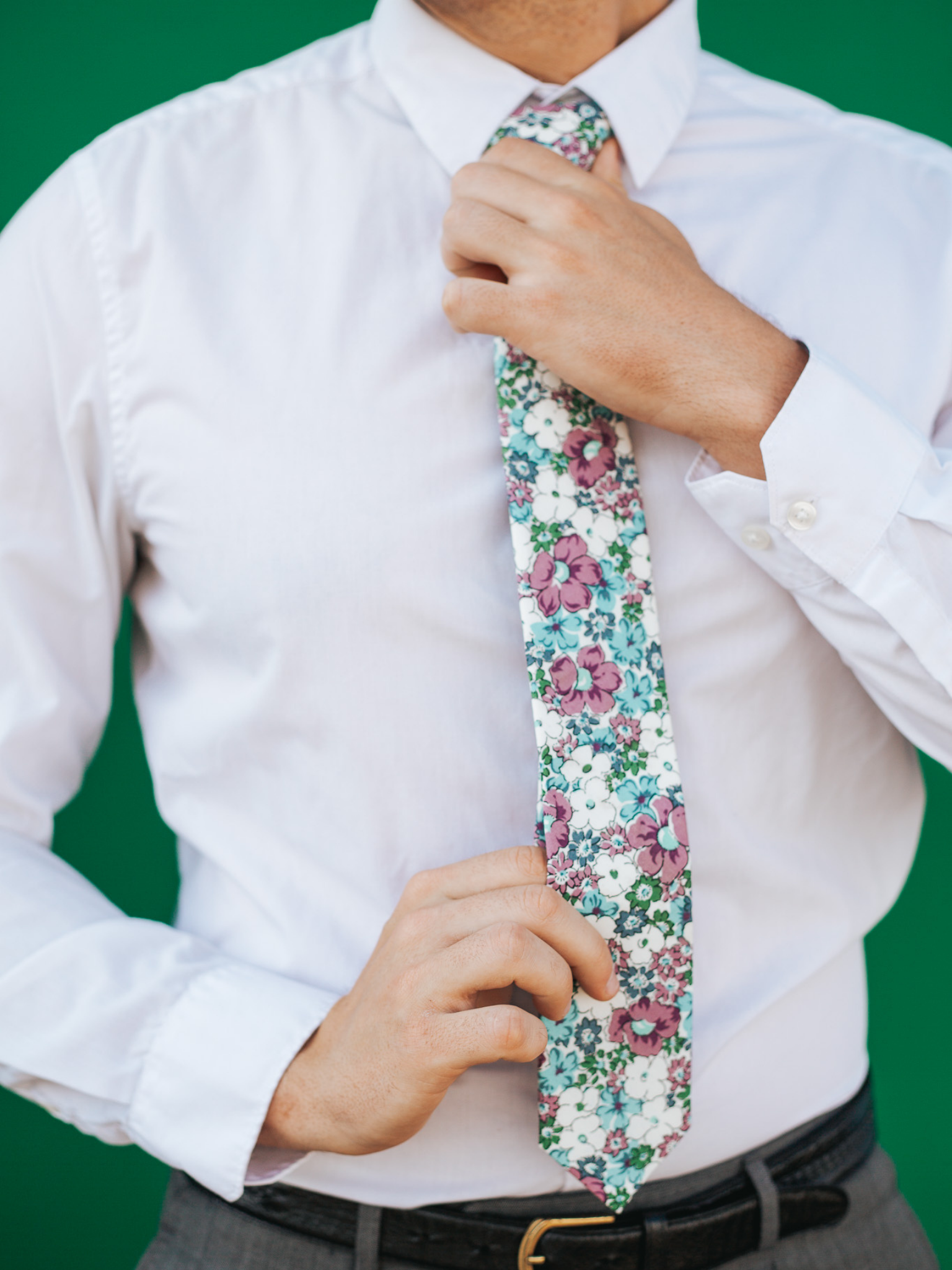 A close up of a man wearing a purple, white, and blue flower cotton skinny tie for weddings, grooms, and groomsmen.