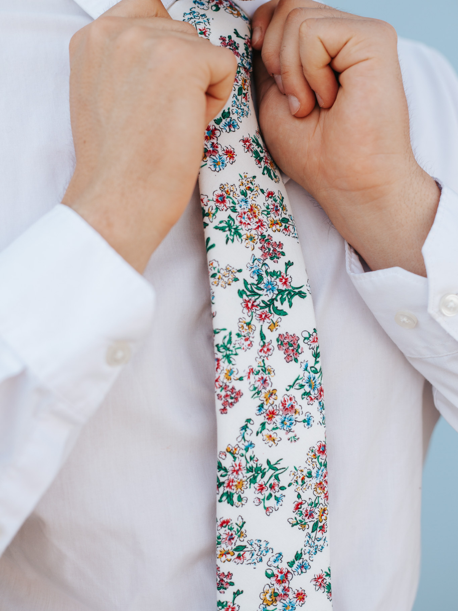 A close up of a man wearing a red, white and blue flower cotton skinny tie for weddings, grooms, and groomsmen.