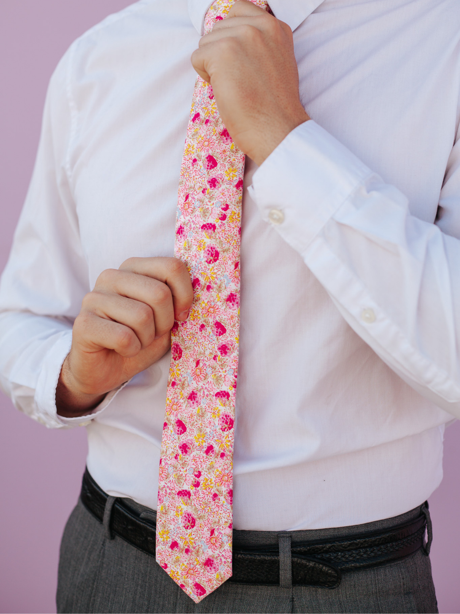 A close up of a man wearing a pink and yellow flower cotton skinny tie for weddings, grooms, and groomsmen.