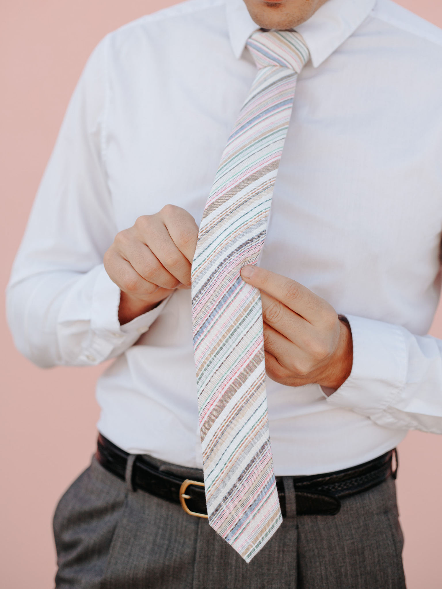 A close up of a man wearing a pink and light blue striped cotton skinny tie for weddings, grooms, and groomsmen.