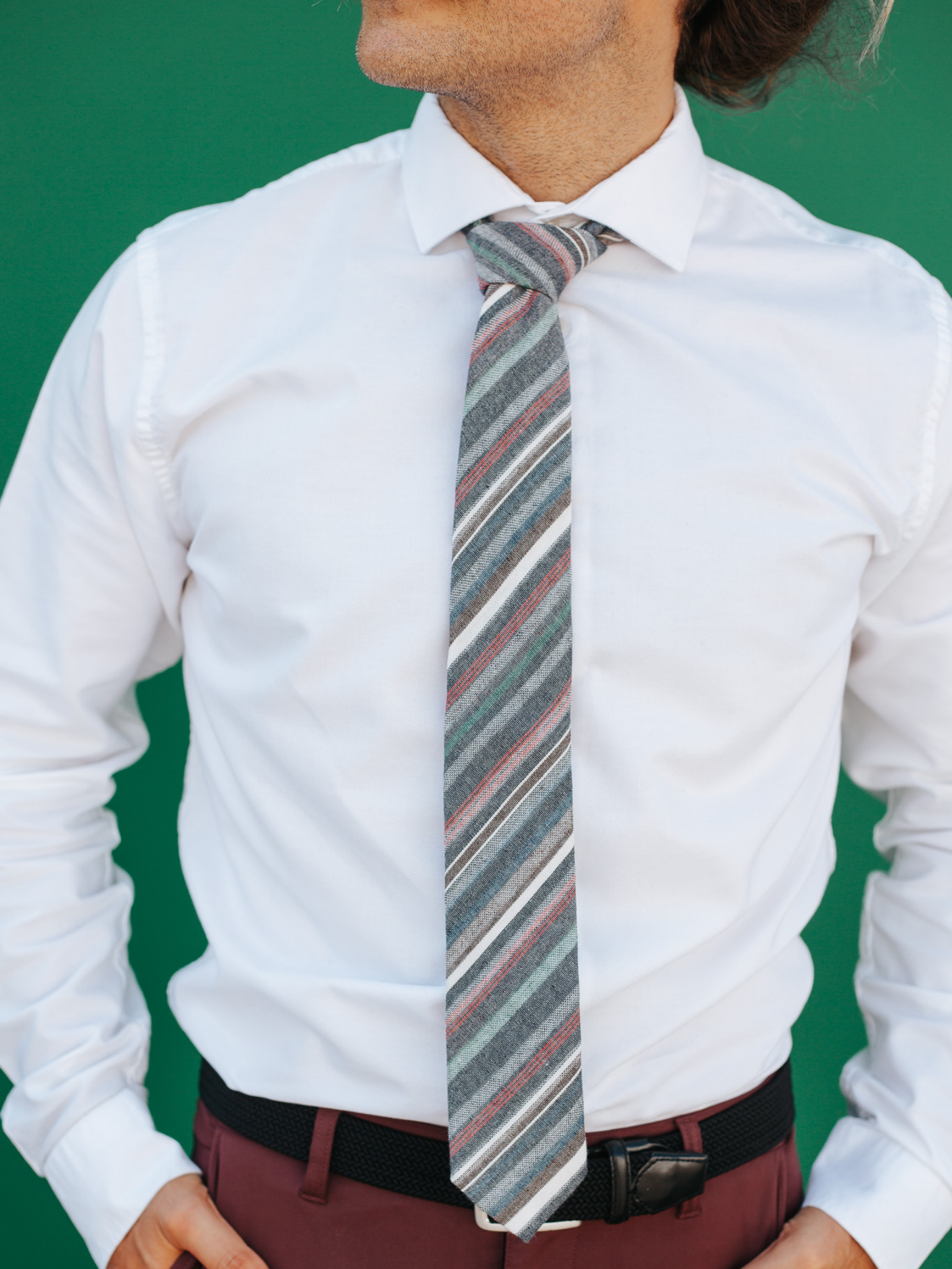 A close up of a man wearing a gray, green, and red striped cotton skinny tie for weddings, grooms, and groomsmen.