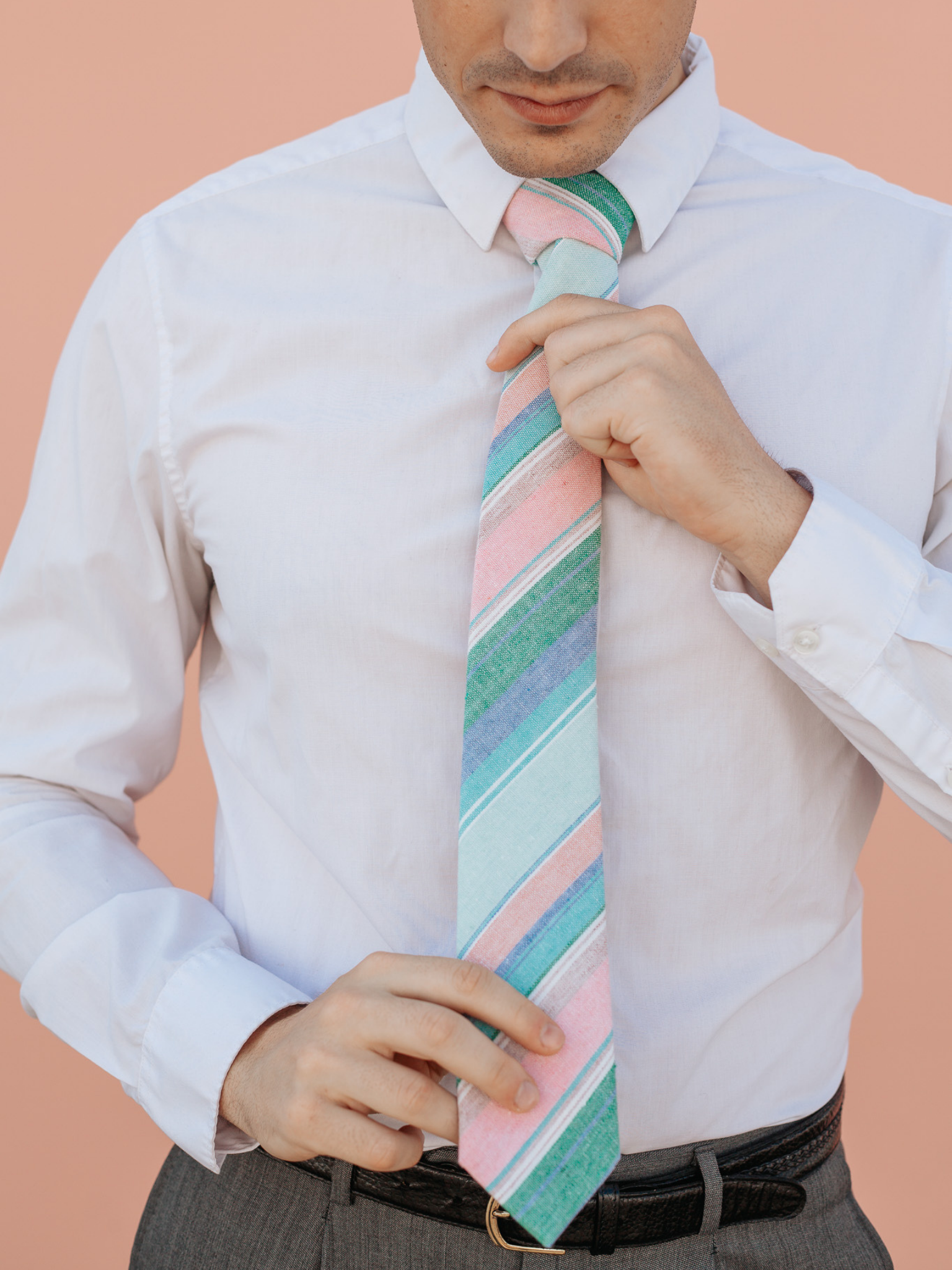 A close up of a man wearing a light pink and blue striped cotton skinny tie for weddings, grooms, and groomsmen.