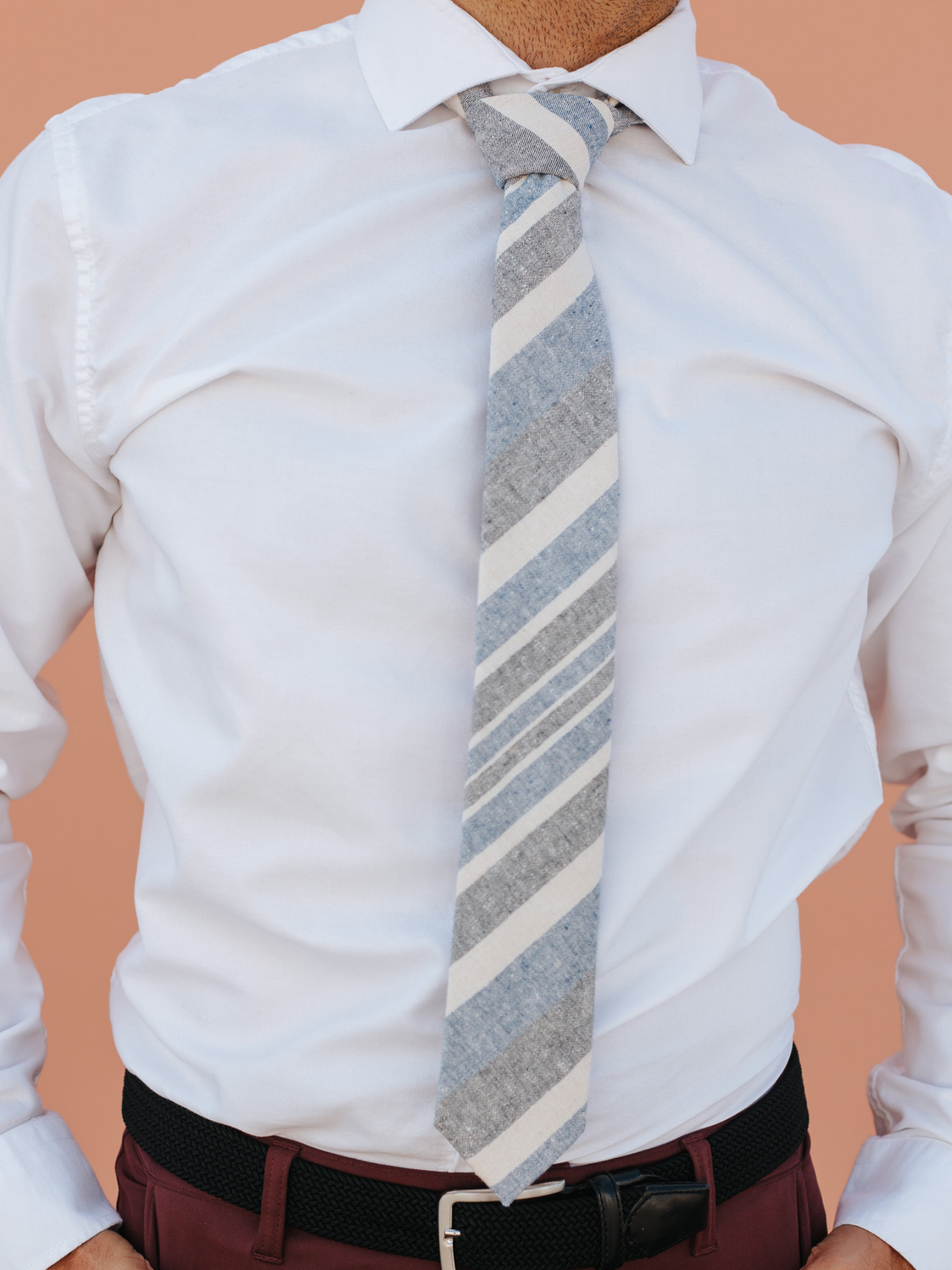 A close up of a man wearing a blue, beige, and gray striped cotton skinny tie for weddings, grooms, and groomsmen.