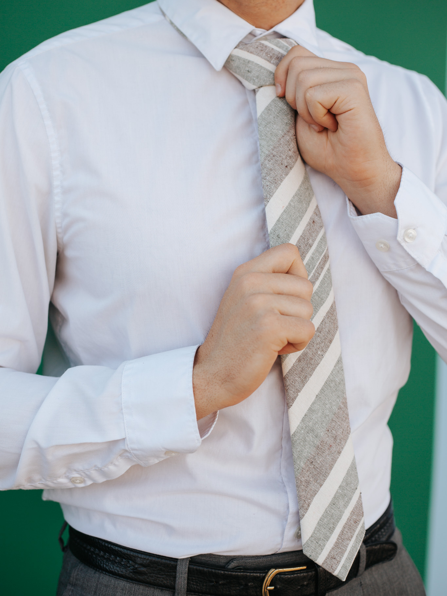 A close up of a man wearing a olive and cream striped cotton skinny tie for weddings, grooms, and groomsmen.