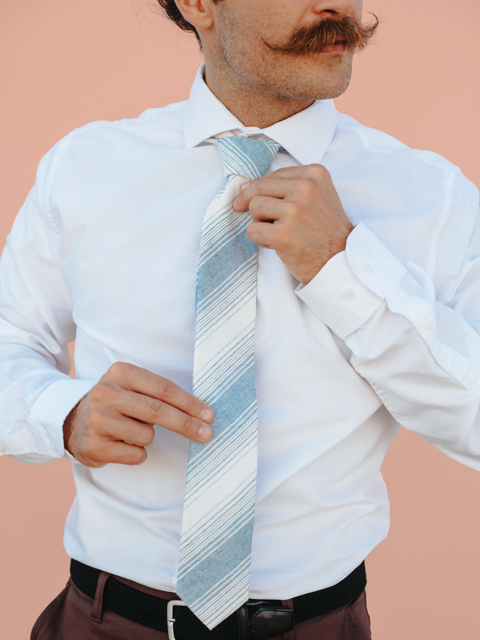 A close up of a man wearing a light blue and beige striped cotton skinny tie for weddings, grooms, and groomsmen.