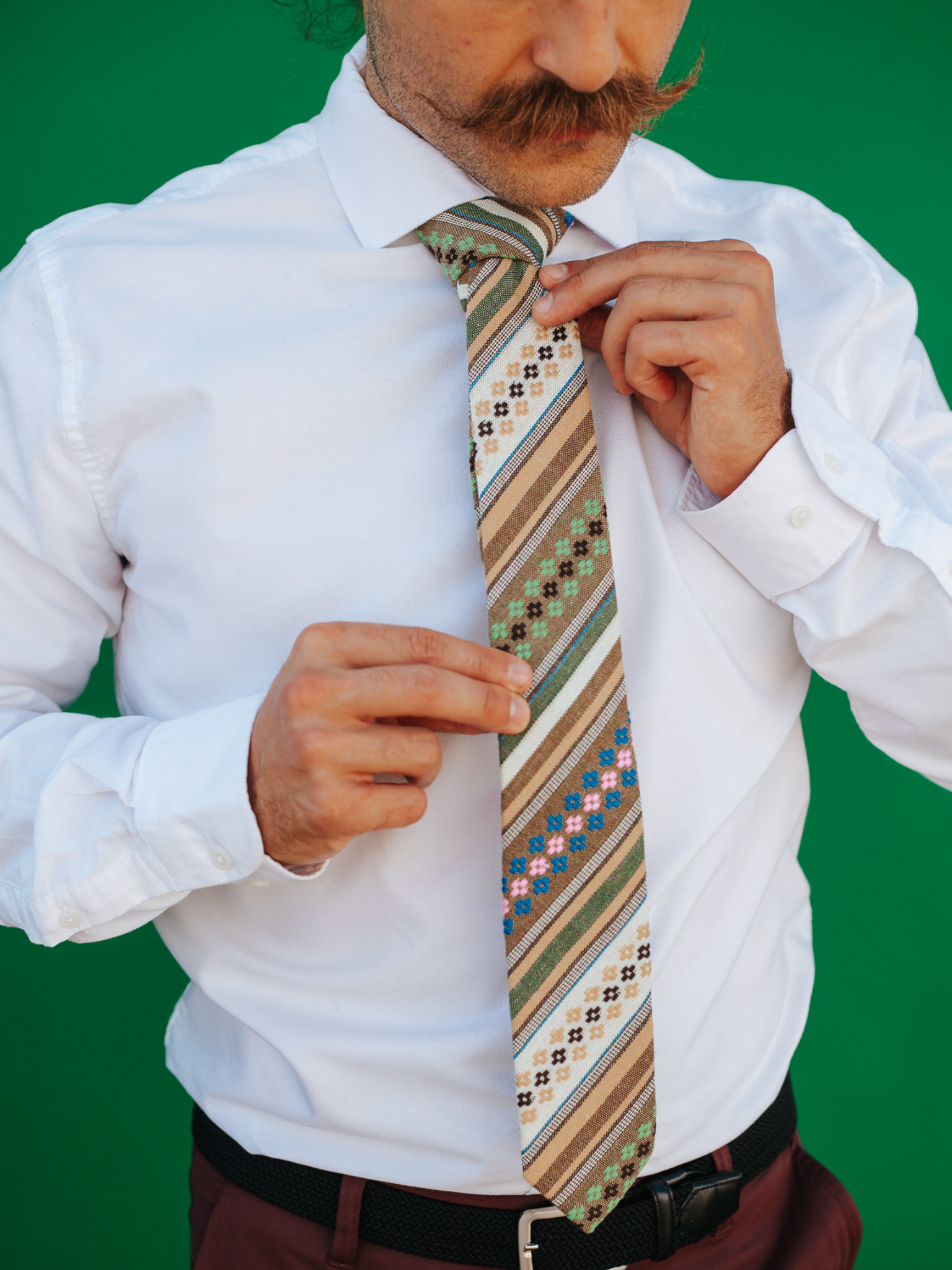 A close up of a man wearing a green, tan, and brown striped cotton skinny tie for weddings, grooms, and groomsmen.