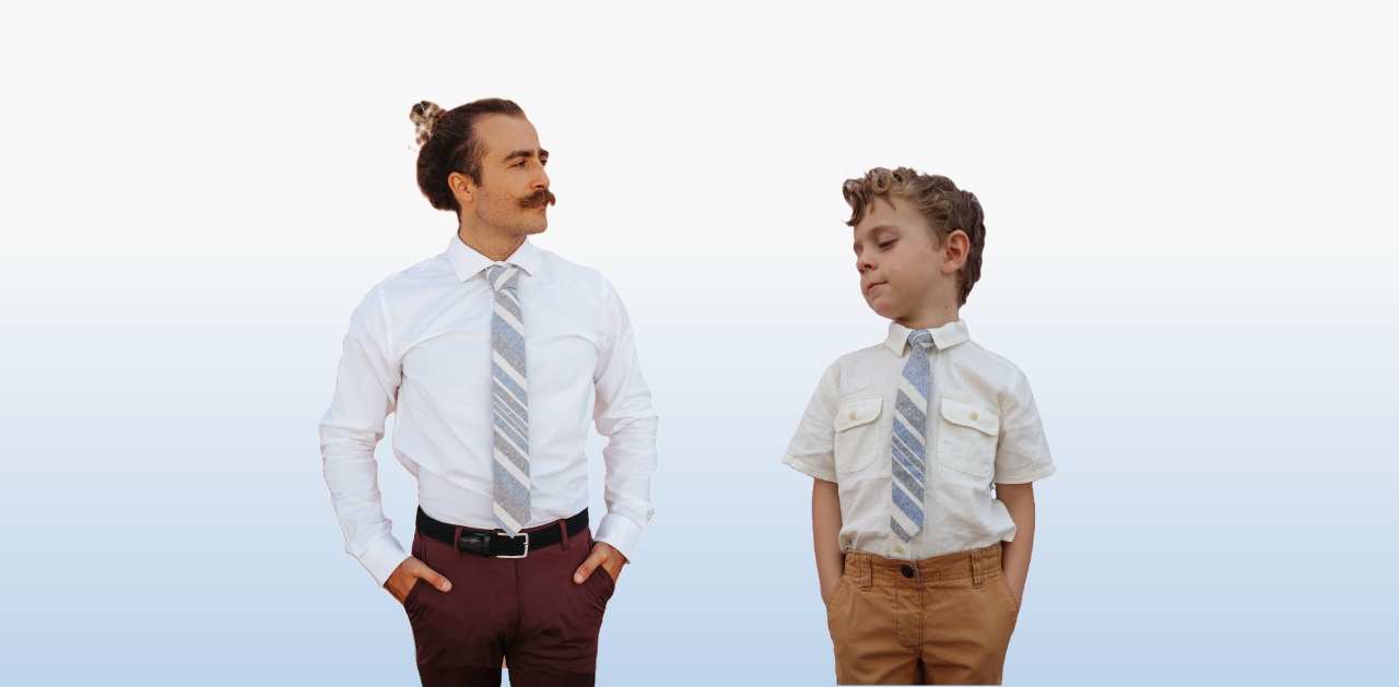 A man and boy in matching blue striped ties by Otis and Oliver standing in front of a blue background. 