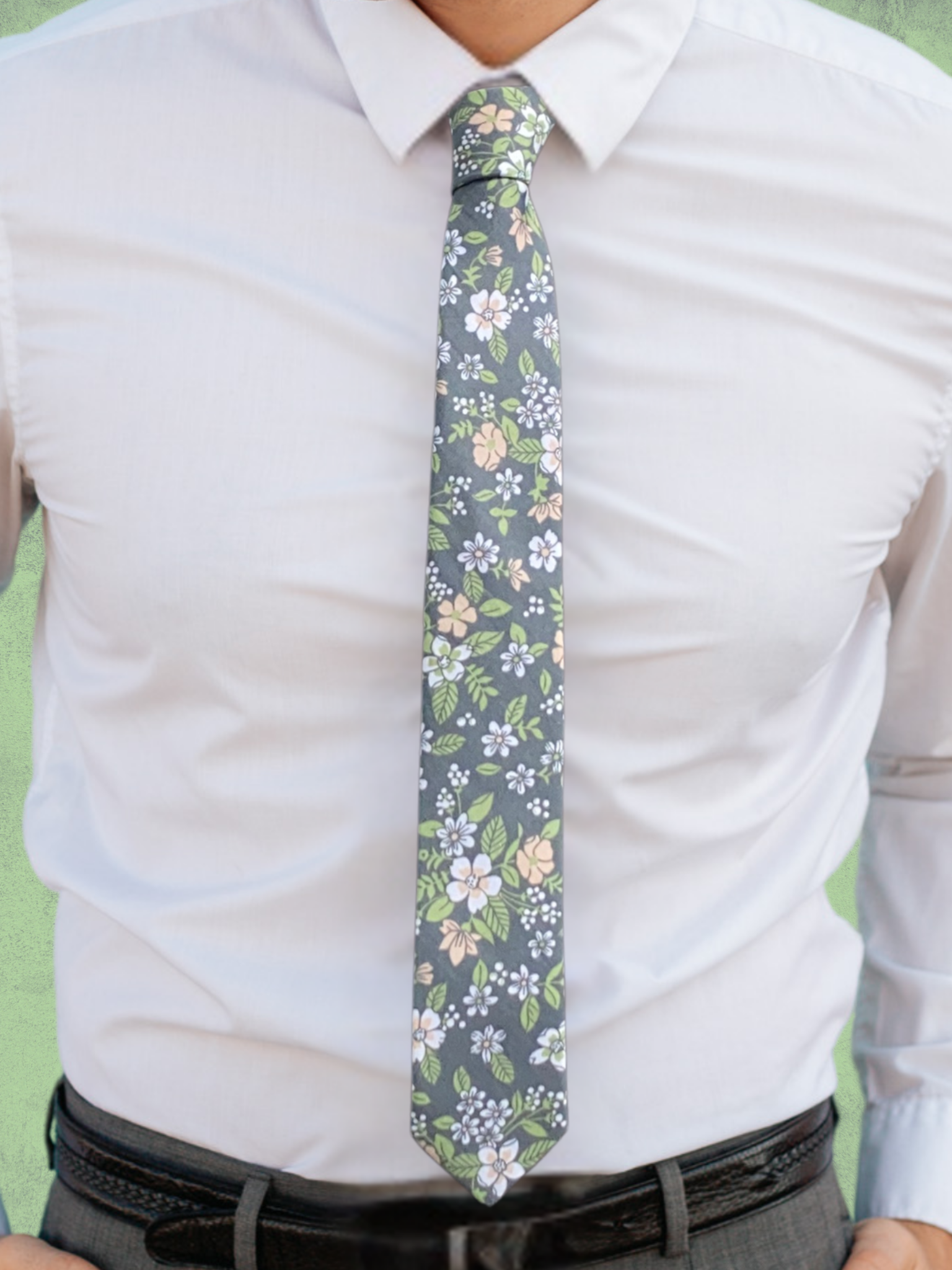 A close up of a man wearing a gray, white, pink petals, and pastel green flower cotton tie for weddings grooms and groomsmen.