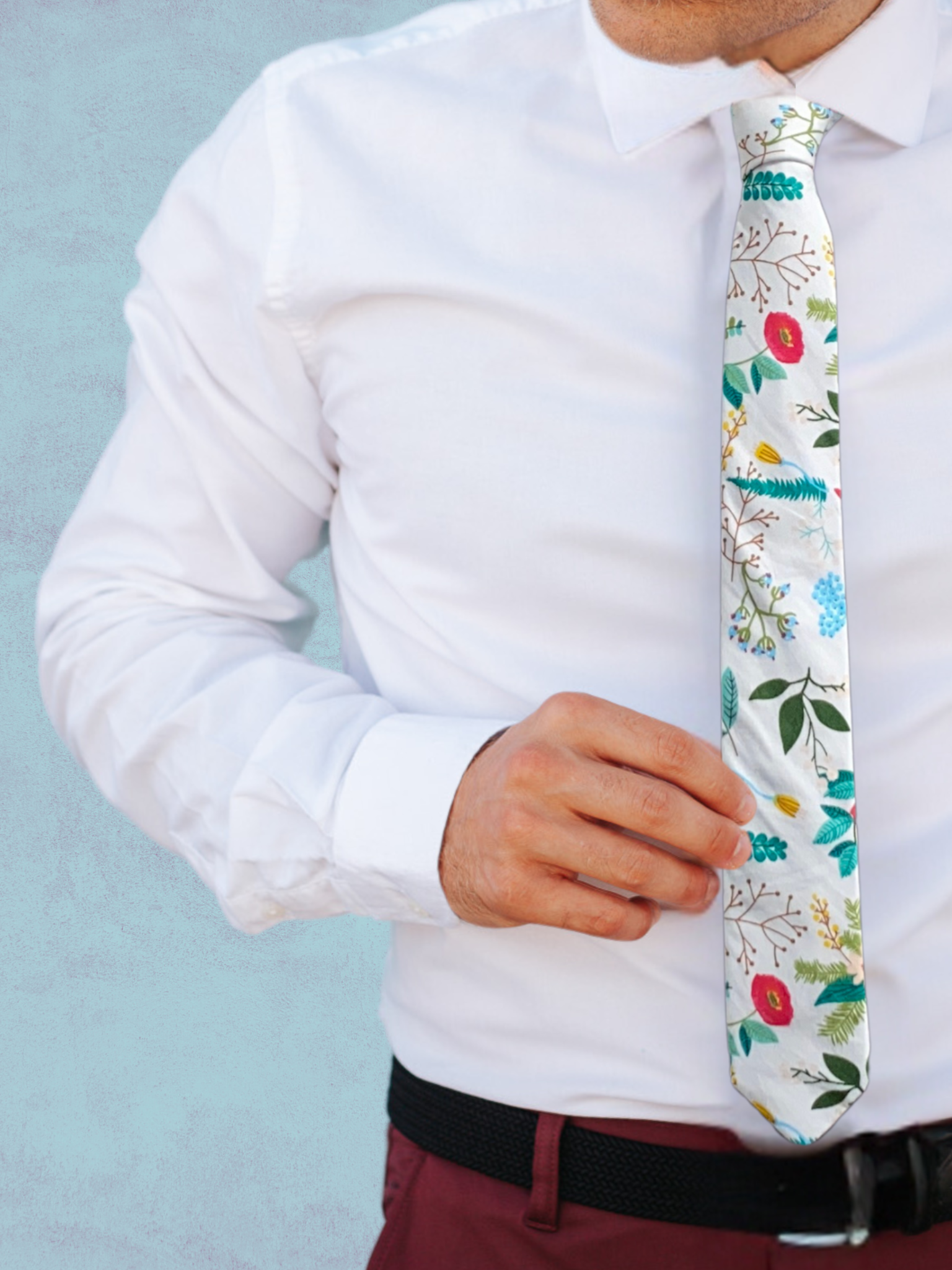 A close up of a man wearing a white, red, brown, and pale green flower cotton skinny tie for weddings, grooms, and groomsmen.