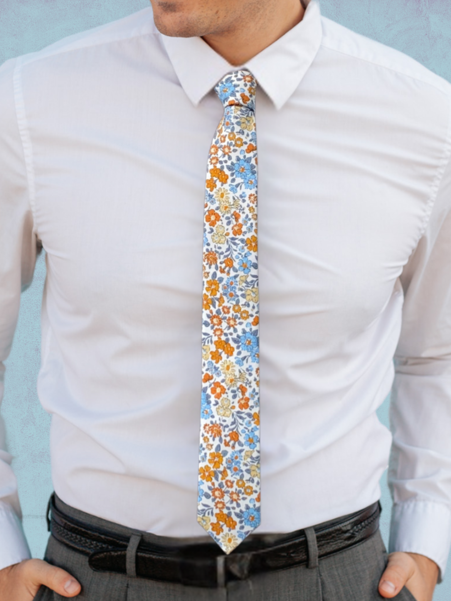 A close up of a man wearing a white, dark orange, pale blue, and yellow flower cotton tie for weddings grooms and groomsmen.